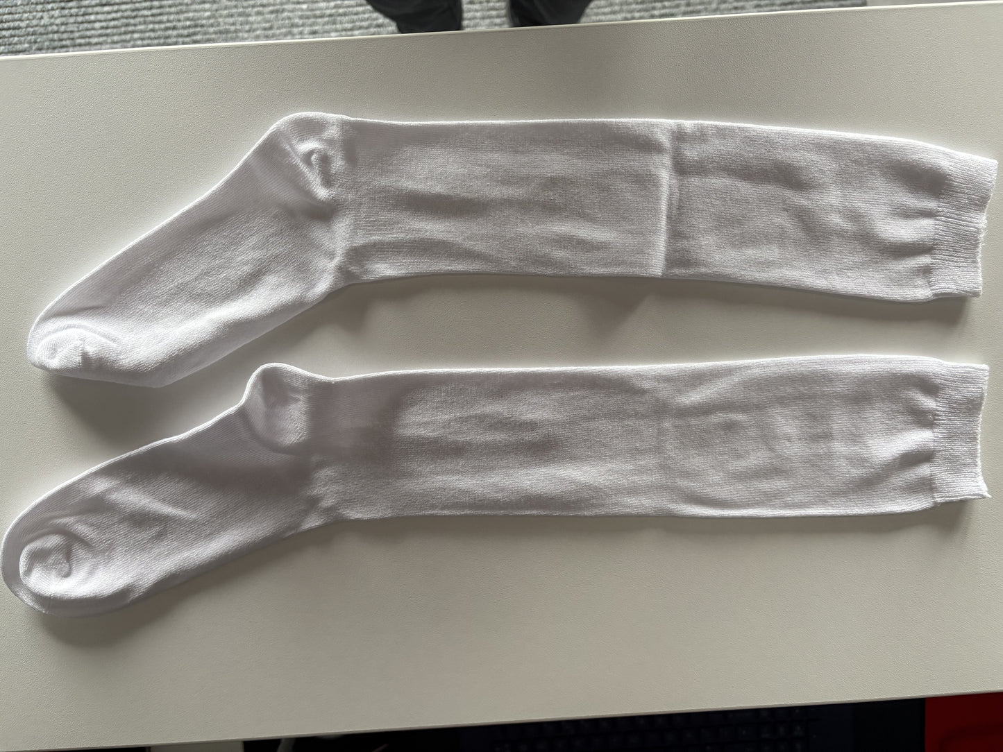 Pair of white knee-high socks on a light gray surface