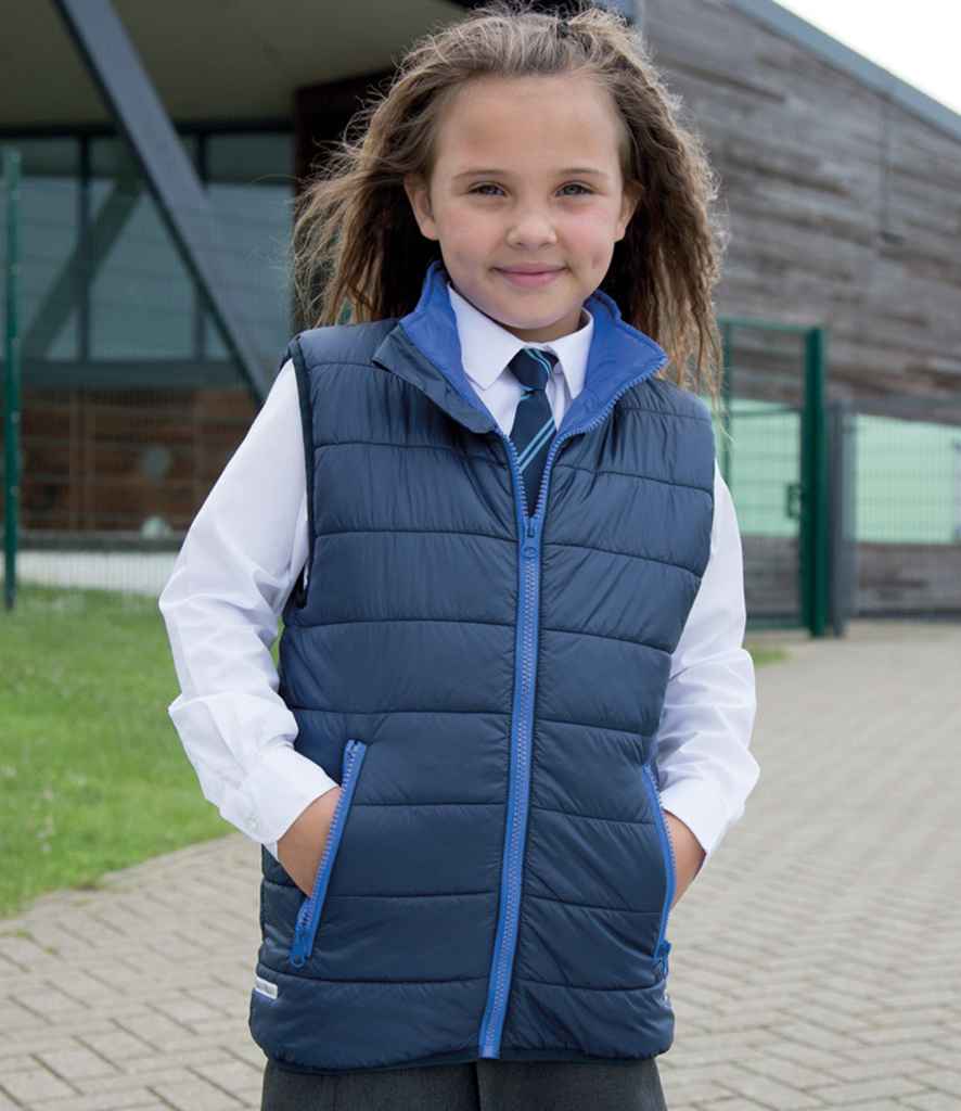 Young girl wearing a blue puffer vest and tie outdoors.